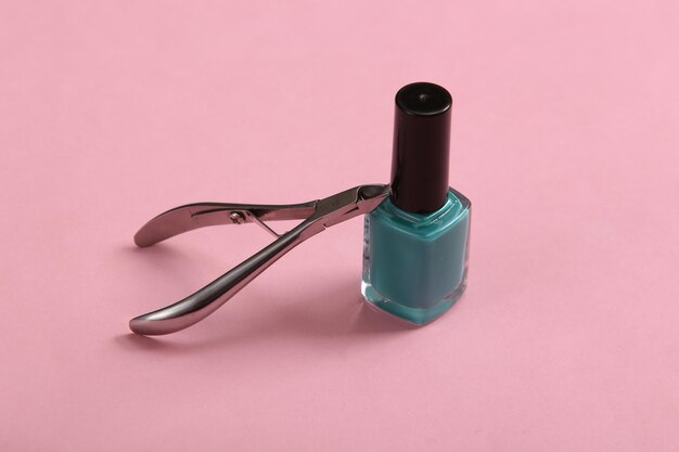 Metal nail pliers and nail polish bottle on pink background Beauty still life