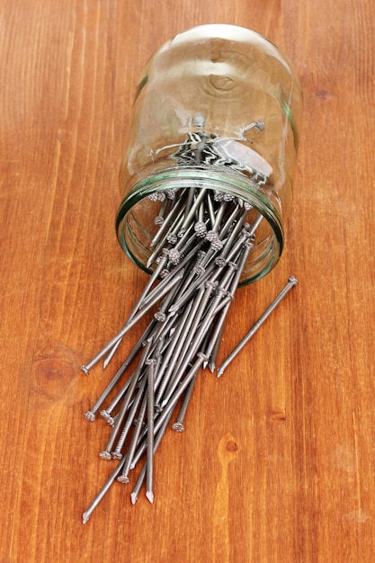 Metal nails and glass jar on wooden background