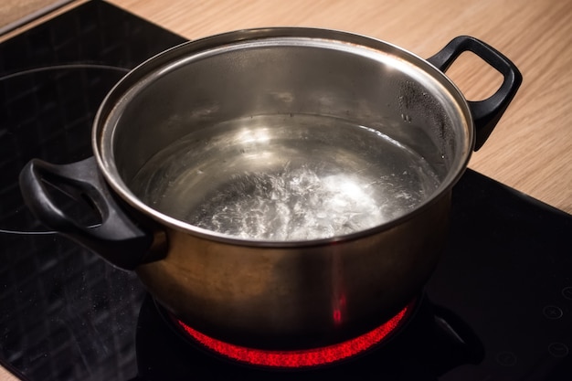 電磁調理器の赤いホットプレートに沸騰したお湯が入った金属製の鍋。