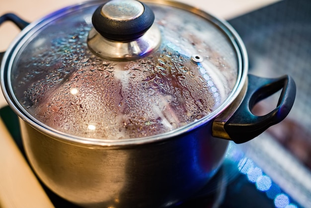 Photo metal pan with misted lid water droplets on the dishes during cooking on the electric stove close up the view from the top