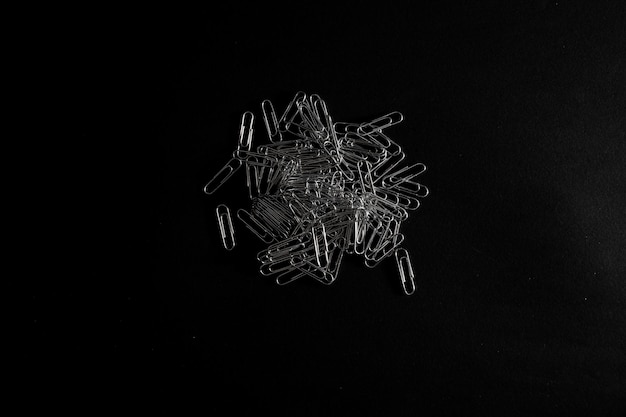 Metal paper clips lie on a black background