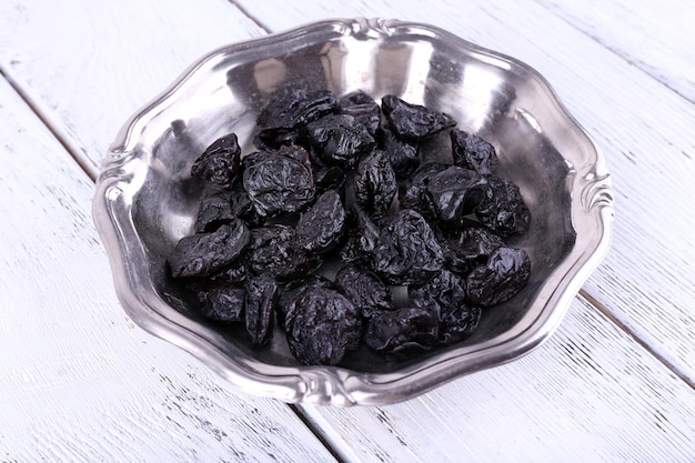 metal plate of prunes on color wooden background