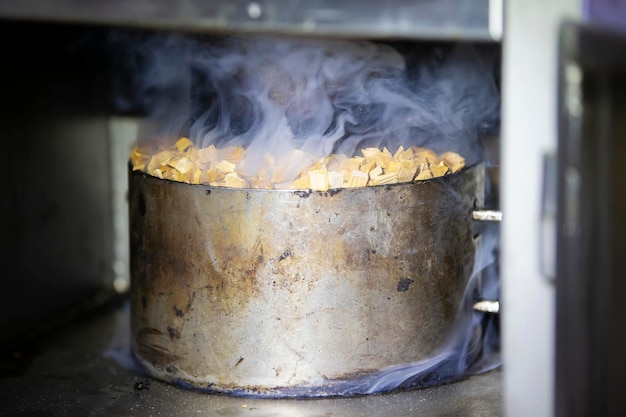 Pentola di metallo con segatura e fumo in un forno industriale per  affumicare il pesce