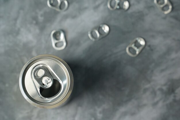 Metal pull tabs of beverage can on gray table.