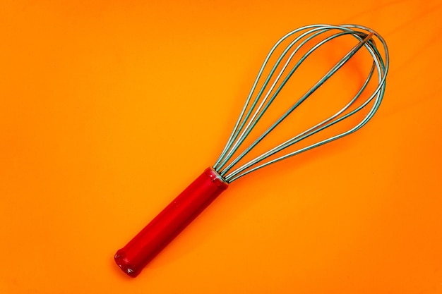 Metal rod whisk with wooden handle insulated on orange background