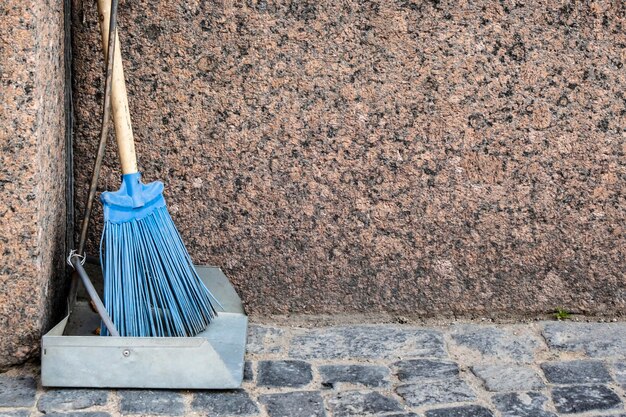 Metal scoop and a plastic broom with a wooden handle stand on a urban cobblestone pavement