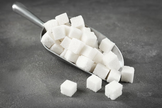 Metal scoop with sugar cubes on grey table