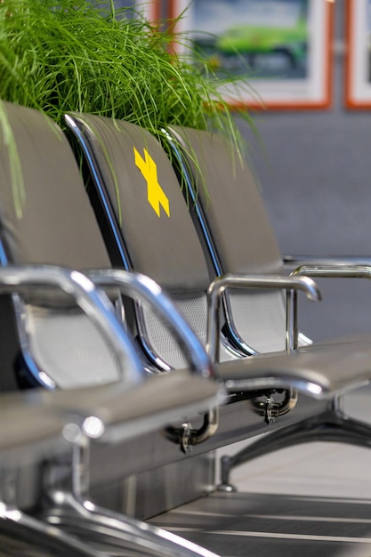 Metal seat section at the airport with a yellow cross sticker.A call for social distancing.Journey