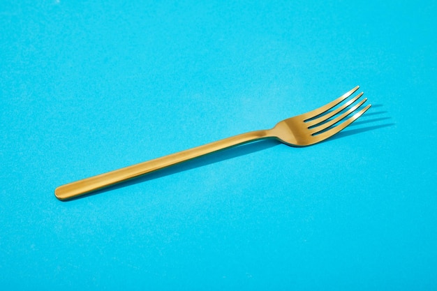 Metal shiny golden fork on blue background