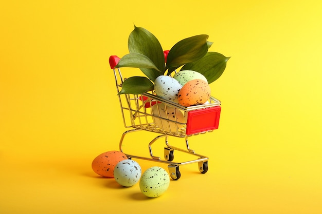 Metal shopping basket with fresh greenery and colorful eggs in it.Easter concept.Colorful and bright background.