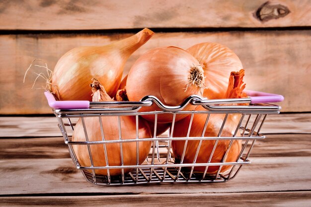 Metal shopping basket with onion on wooden table.