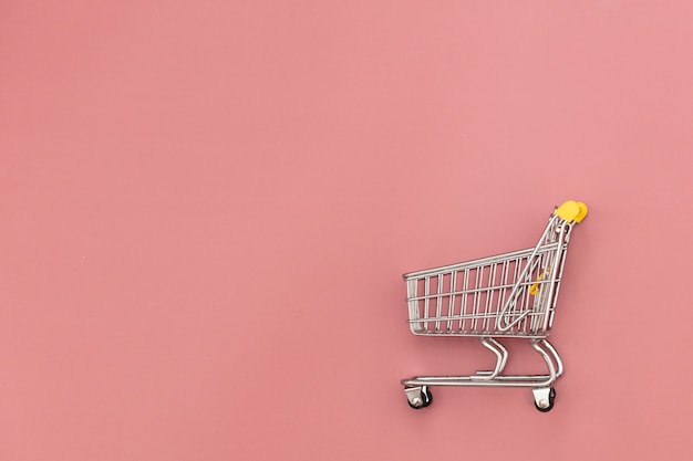 Metal shopping cart on pink background.