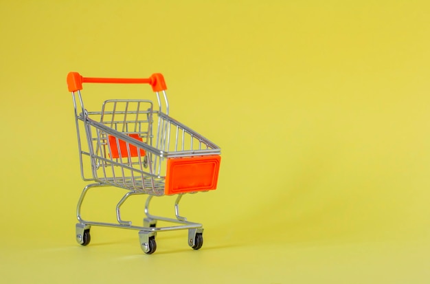 Metal shopping cart on a yellow background with a place to copy A symbol of trade and sales