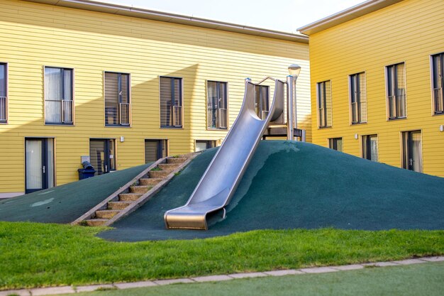 A metal slide on a children's playground with a green lawn Stairs to the hill Yellow House