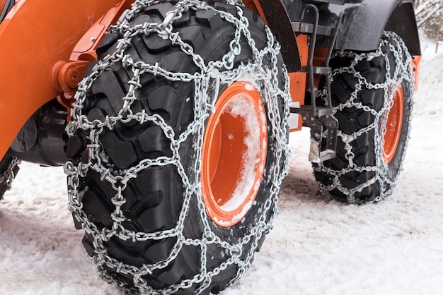 Metal snow chains wrapped around wheel tires of bulldozer car parked on snowy road