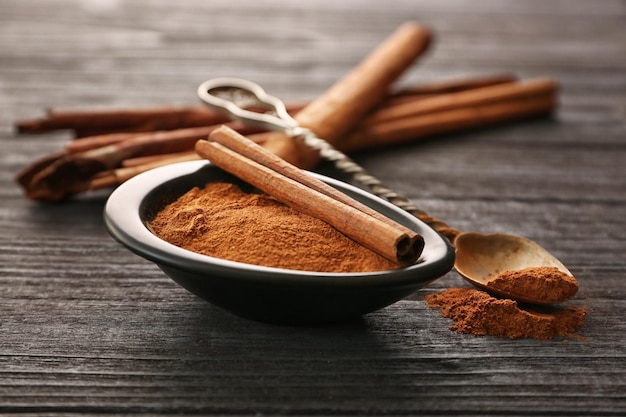 Metal spoon ceramic bowl with cinnamon sticks and powder on wooden table