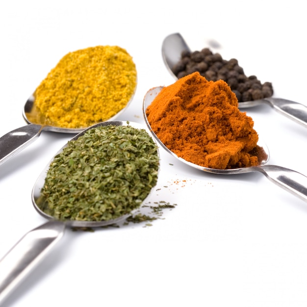 Metal spoons with various ground spices on white background