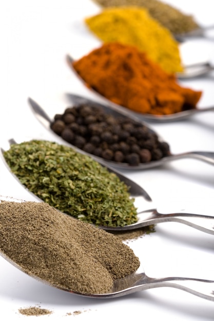 Metal spoons with various ground spices on white background