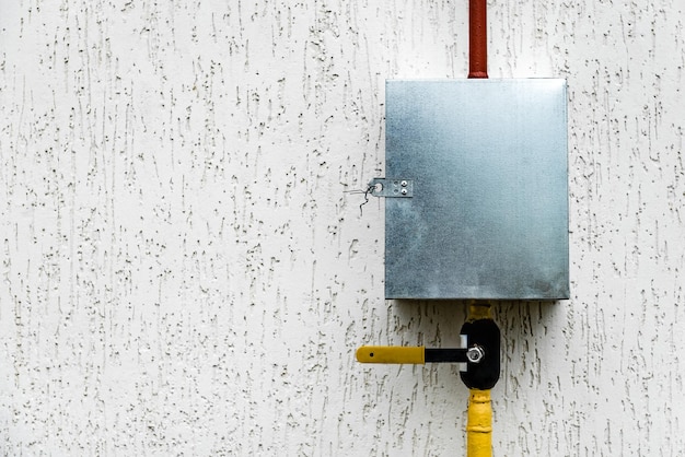 Metal steel gas meter box with connecting yellow pipes hanging on exterior house wall.