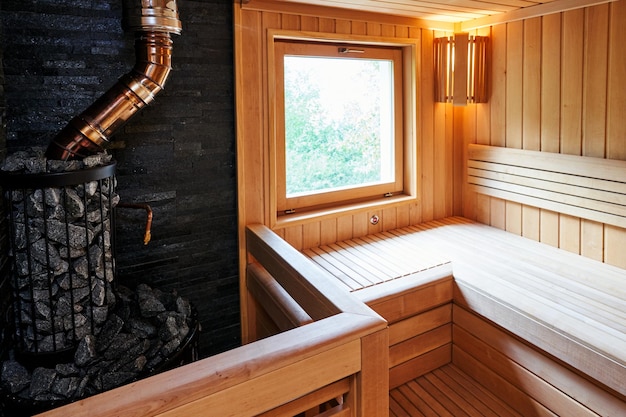 Foto cuoco metallico pieno di pietre con un camino nella sauna vicino alle panchine di legno accanto alla finestra