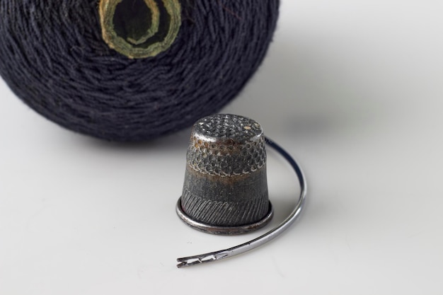 Metal thimble sewing needle and spool of black thread on a white background