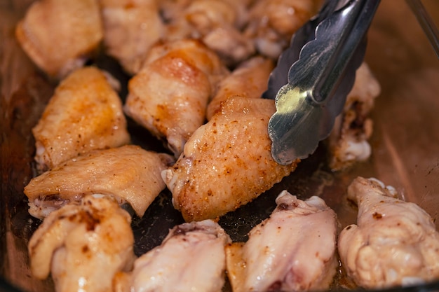 Photo metal tongs pick up a baked chicken wing from a plate cooking healthy food