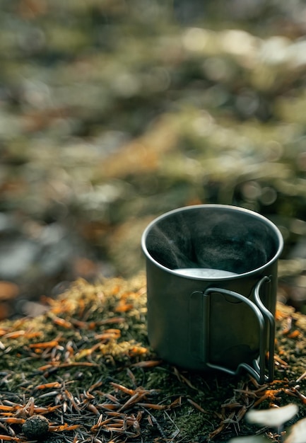 Metal tourist cup steaming with a hot beverage in the woods