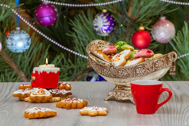 Metal vase with gingerbread cookies and fir tree with toy balls on the background