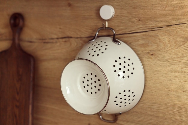 Metal white colander hanged on hook on a kitchen wooden wall.