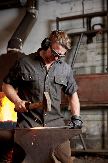 Metal worker using a hammer to shape a red hot piece of metal on an anvil