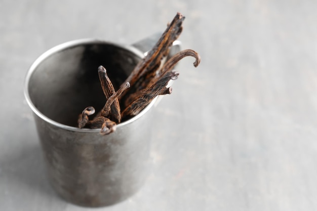 Foto metalen beker met gedroogde vanillestokjes op grijze tafel