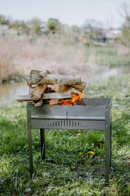 Metalen draagbare barbecue met brandend brandhout en rode vlammen