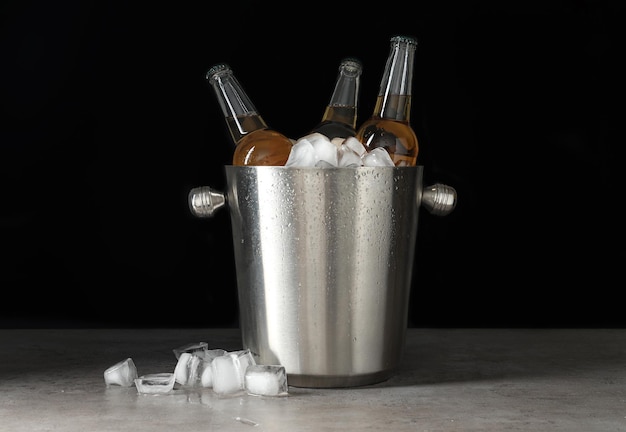 Metalen emmer met flesjes bier en ijsblokjes op grijze tafel