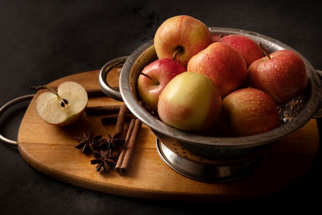 Metalen kom vol rode rijpe appels verspreid kaneelstokjes anijs sterren een halve appel op houten snijplank stilleven Appeltaart ingrediënten Thuis koken