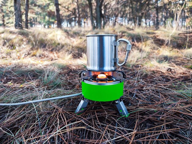 Metalen kop hete thee of koffie op draagbare gasbrander of campingkachel vuur buiten. ecotoerisme en wandelconcept