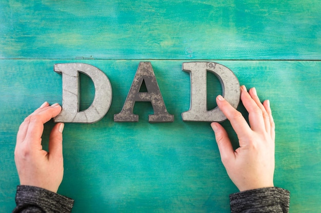 Metalen letters DAD op een geschilderde houten ondergrond.