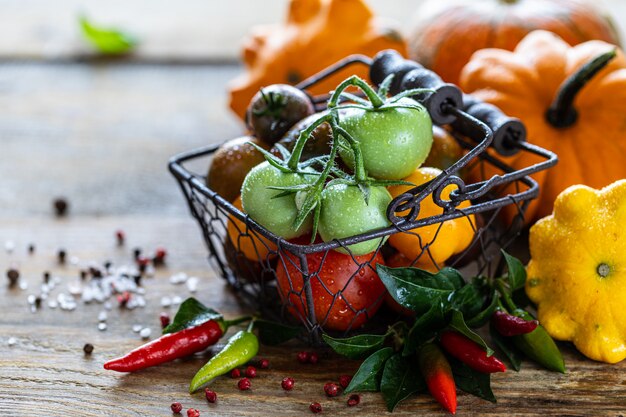 Metalen mand met rijpe verschillende rode, gele en groene tomaten op een houten tafel en basilicum bladeren