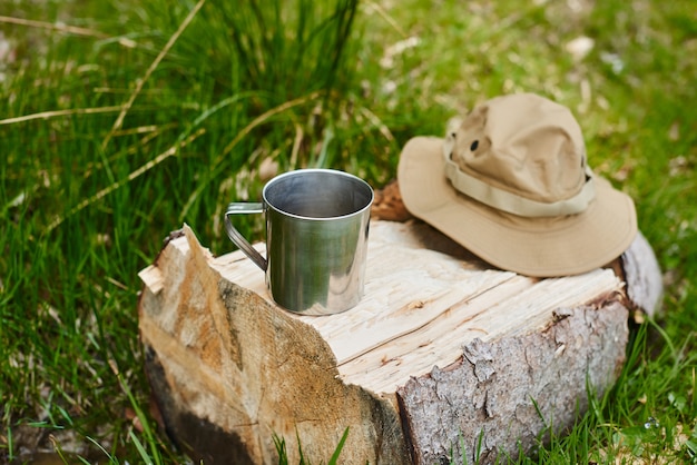 metalen mok en toeristische hoed met velden liggen op een log in het bos
