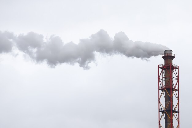 Metalen pijp waar witte rook uit komt tegen de grijze lucht