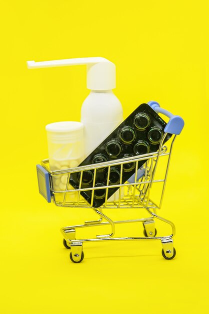 Metalen supermarktwagen met medicijnen: keelspray, pillen op helder geel.