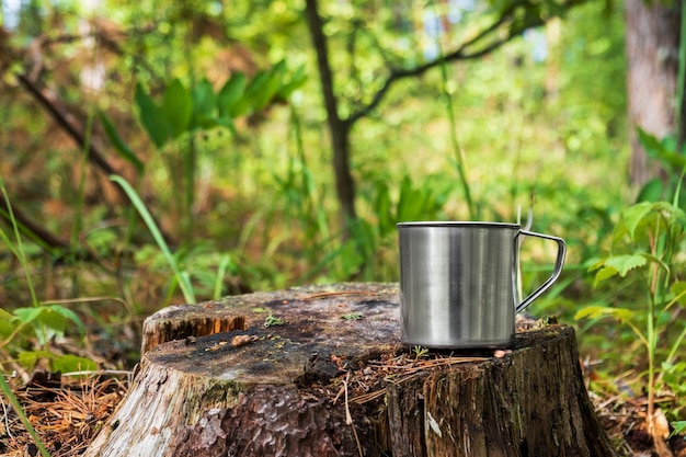 Metalen toeristenmok met warme drank staat op boomstronk in het bos