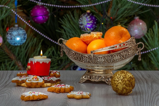 Metalen vaas met sinaasappels en dennenboom met speelgoedballen op de achtergrond