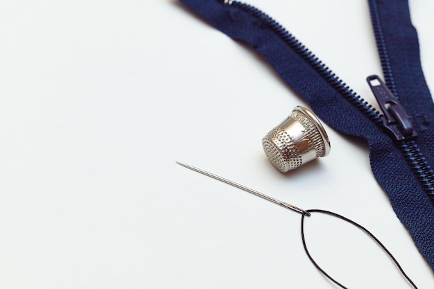 Metalen vingerdraad met een naald en een rits op een witte achtergrond kleding reparatie