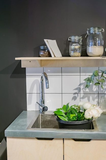 metalen wasbak en verschillende glazen potten op een metalen tafel naast een mand met bloemen