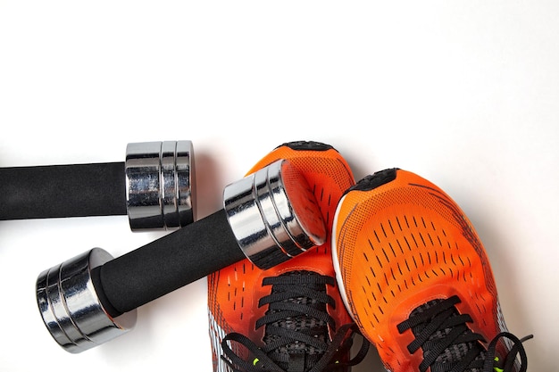 Metallic heavy dumbbell dropped on leg in orange sneaker isolated on white background Top view with copy space