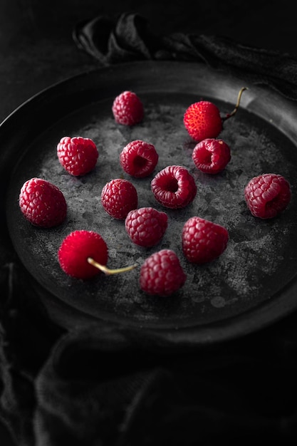 Metallic plate with fresh raspberries. Dark mood food photography with copy space