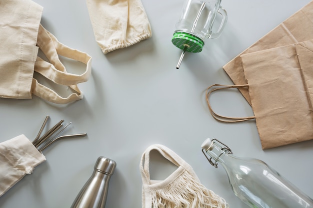 Metallic straws, cotton bag, glass and metal bottle on grey. 