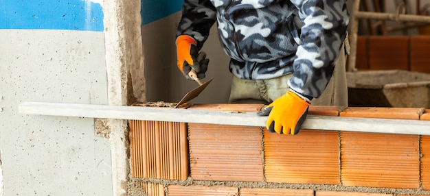 Metselaar die baksteenmetselwerk op binnenlandse muur installeert.