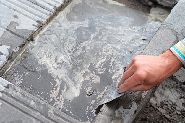 Metselaar die bestratingsplaten legt op een zomerdag Close-up bovenaanzicht van de hand van een bouwer Trottoirreparatie