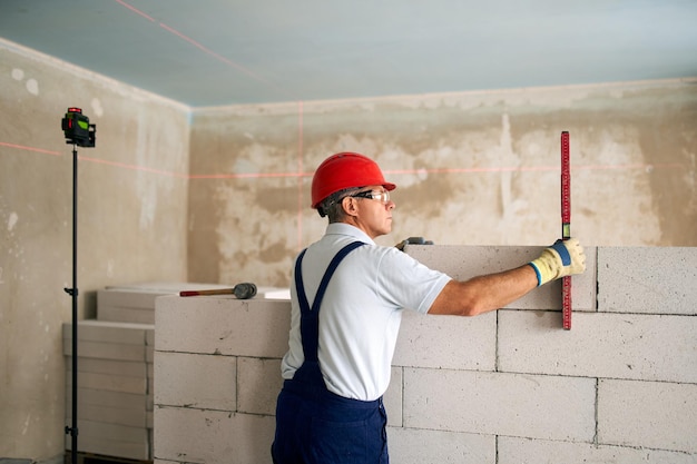 Metselaar die waterpas en laserwaterpas gebruikt om betonblokken op de muuraannemer nauwkeurig te controleren